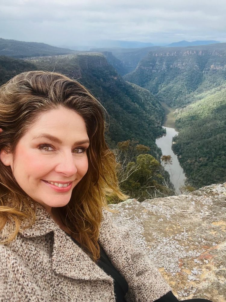 Wedding makeup artist Claudy at Caoura Cliffs in the Southern Highlands, set against the dramatic cliffside landscape
